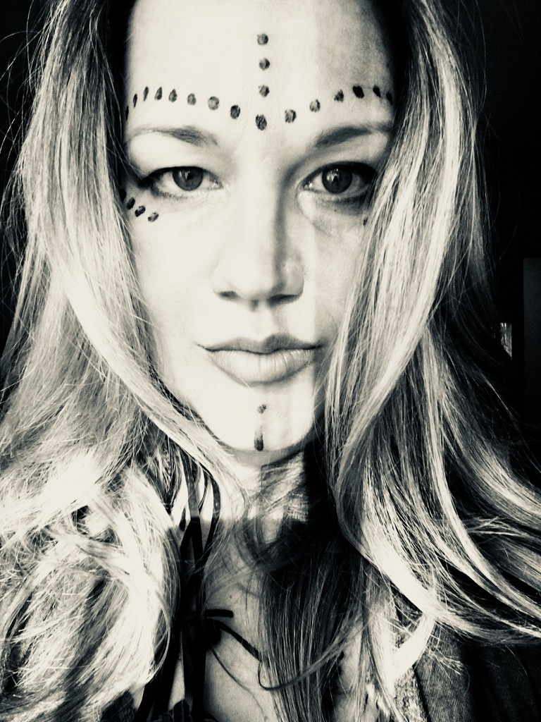 Black and white self portrait of Heather, dotted lines painted across her brow and down her chin, looking straight into the lens.