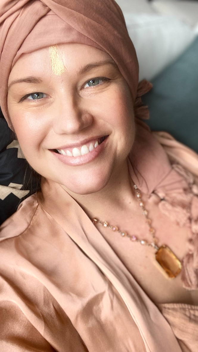 Heather smiling in a rose silk turban and blouse, a streak of gold on her brow and an amber pendant at her chest.