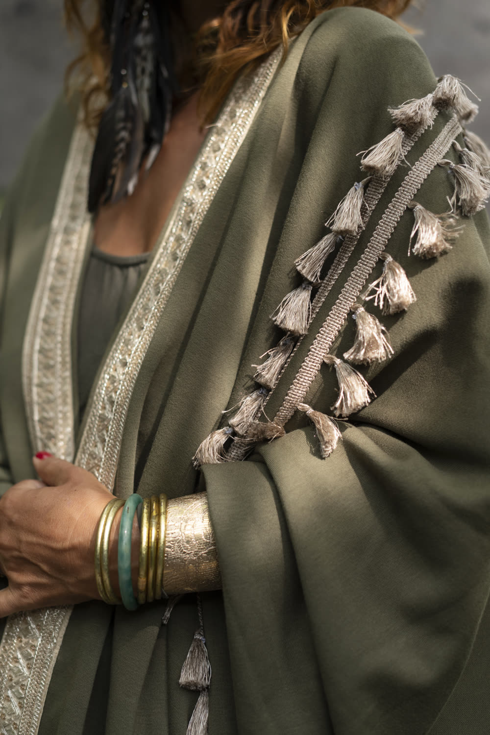 Close detail of an olive fleece sleeve edged in gold, with tassels and stacked bangles.