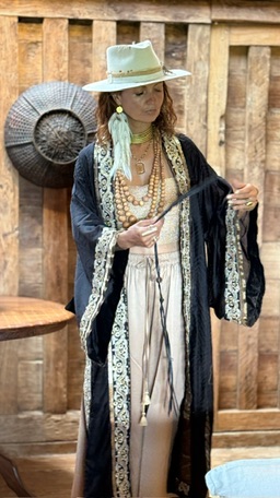 A woman in a white hat and layered beads adjusting a black and cream embroidered kimono.