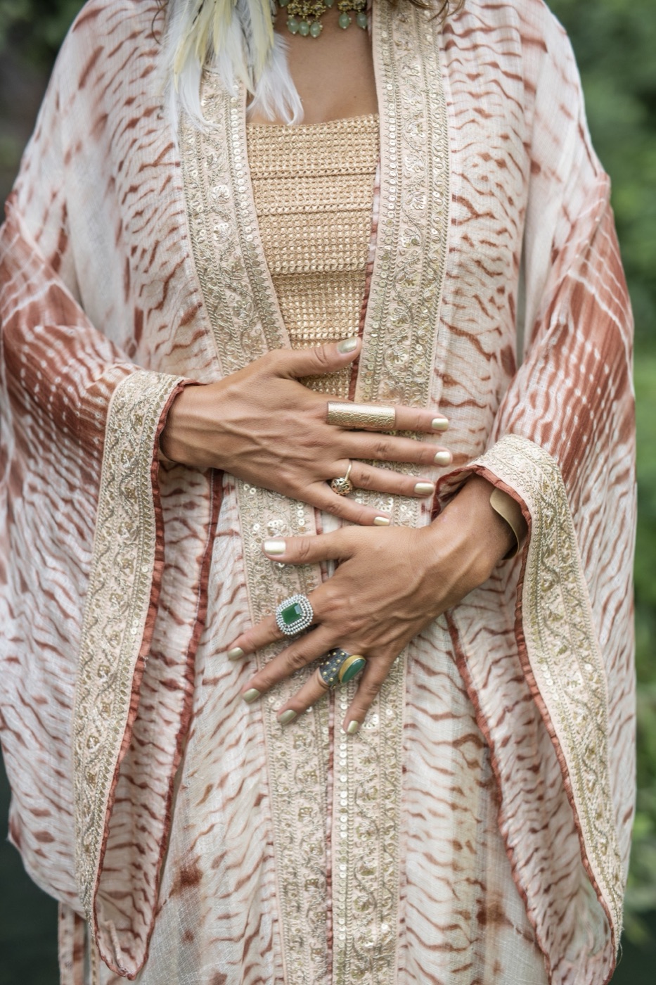 Hands with an emerald ring resting on a rose shibori silk kimono with gold trim.
