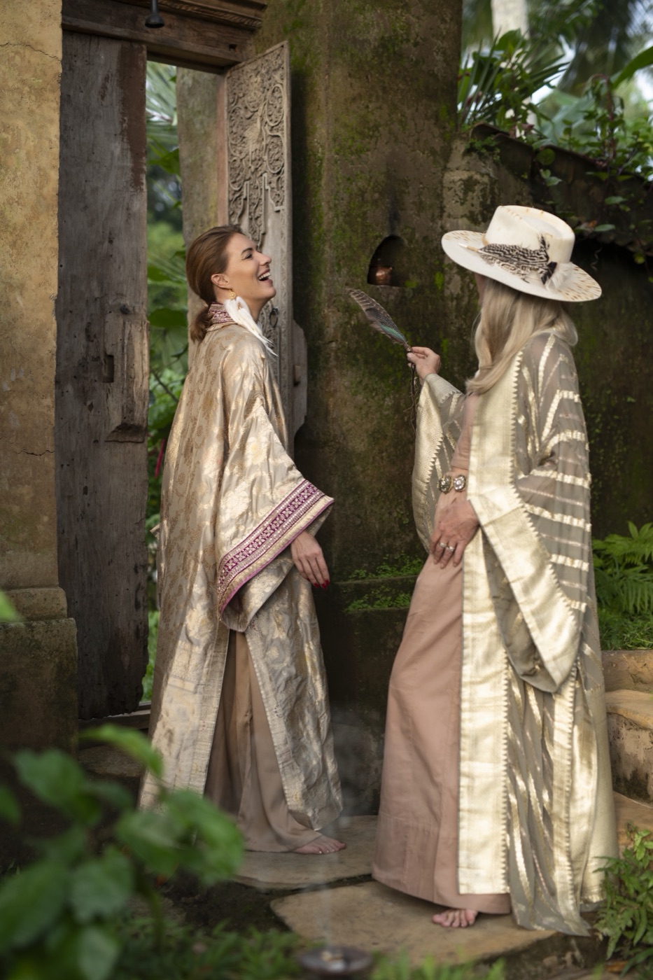 Two women in cream and gold robes laughing beside a carved temple doorway.