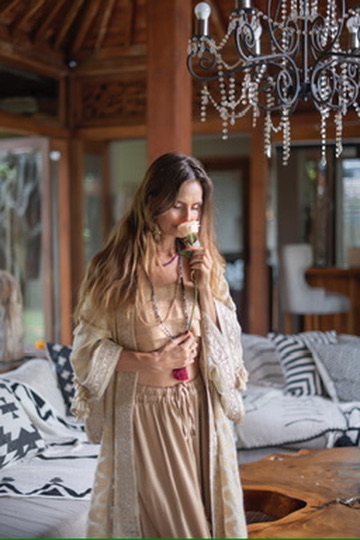 A woman in a cream robe smelling a white rose under a crystal chandelier.
