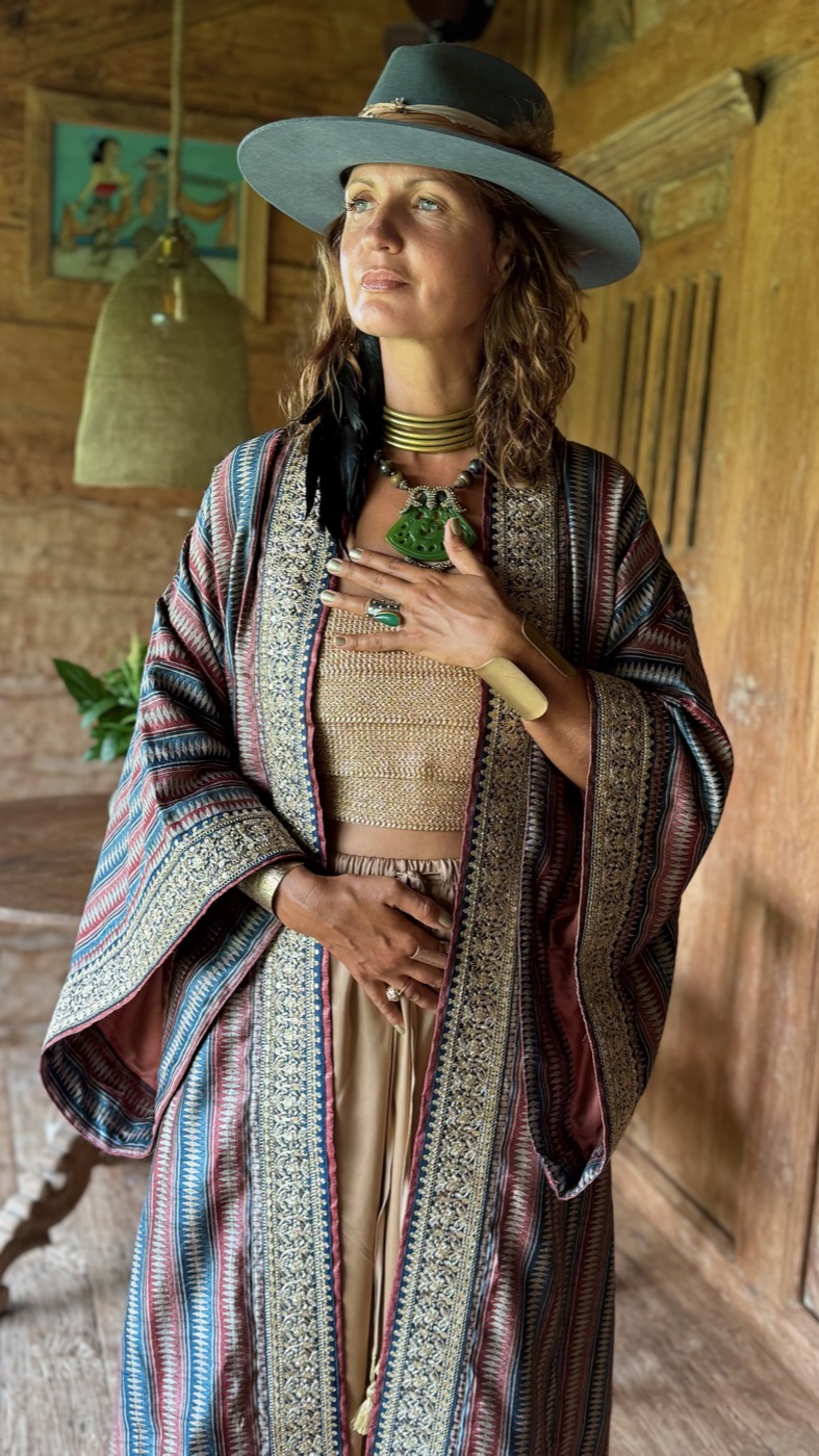 A woman in a hat with eyes closed, a hand on her heart, in a striped silk kimono.