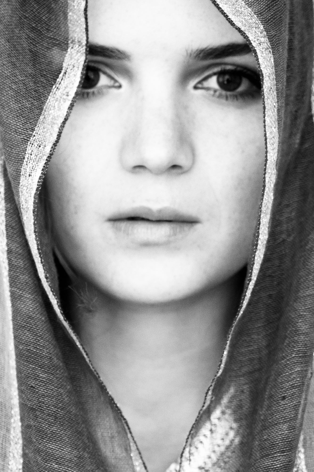 Black and white portrait by Heather Brand: a young woman wrapped in a woven veil, looking straight into the lens, calm and unguarded.